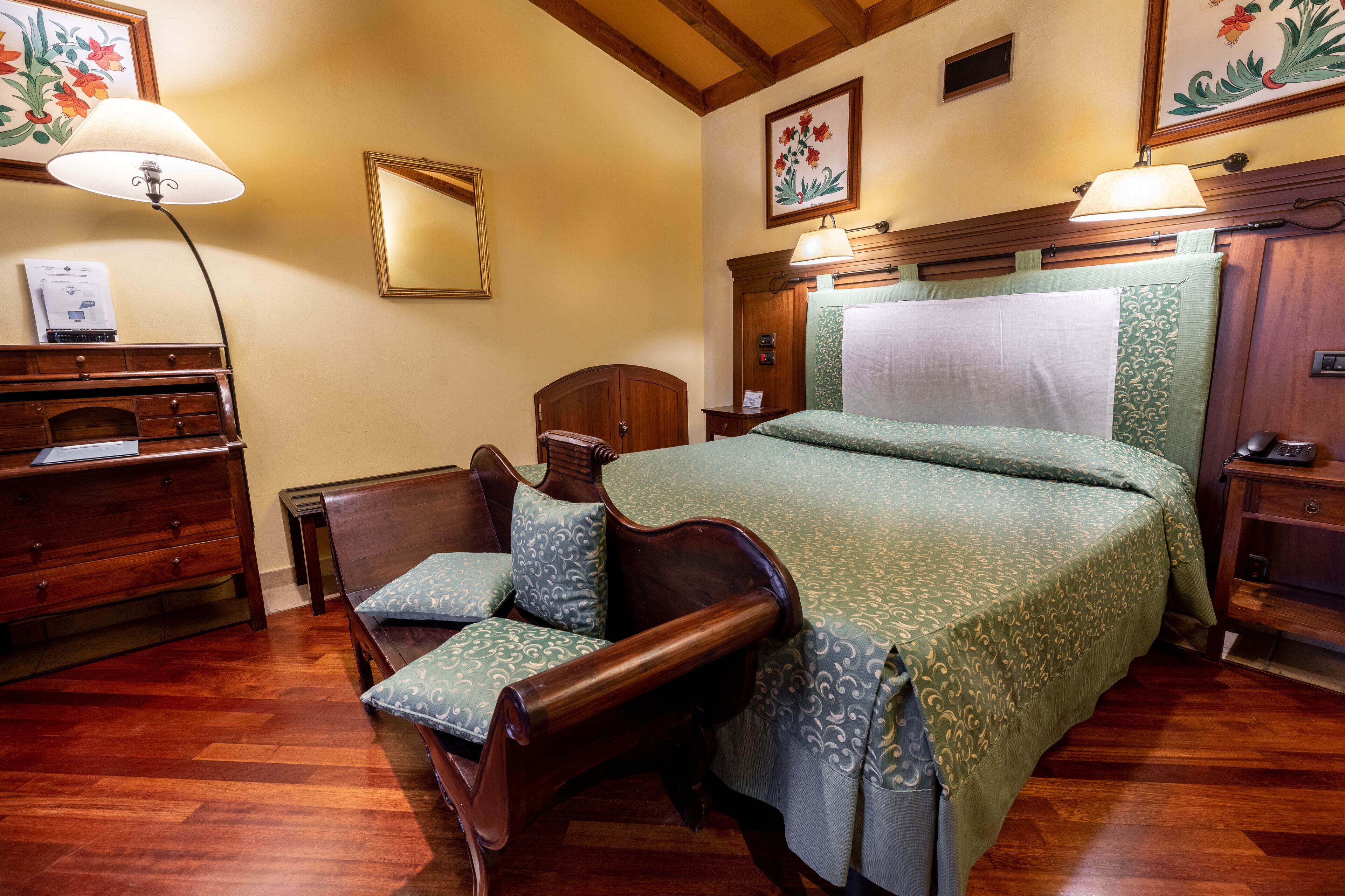A bedroom with a wooden bed, a wooden chair with a cushion, a nightstand, a dresser, and a lamp.