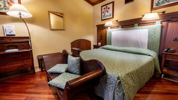 A bedroom with a wooden bed, a wooden chair with a cushion, a nightstand, a dresser, and a lamp.