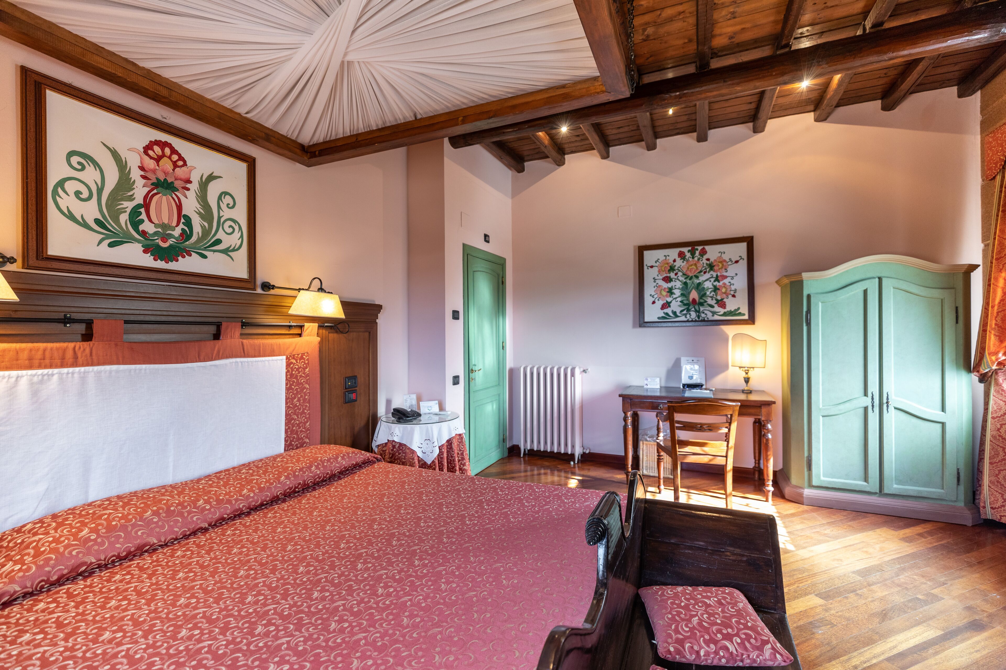 Ein Schlafzimmer mit einem großen Bett, einem hölzernen Kopfteil, einer grünen Tür, einem Schreibtisch mit Lampe und einem Kleiderschrank.