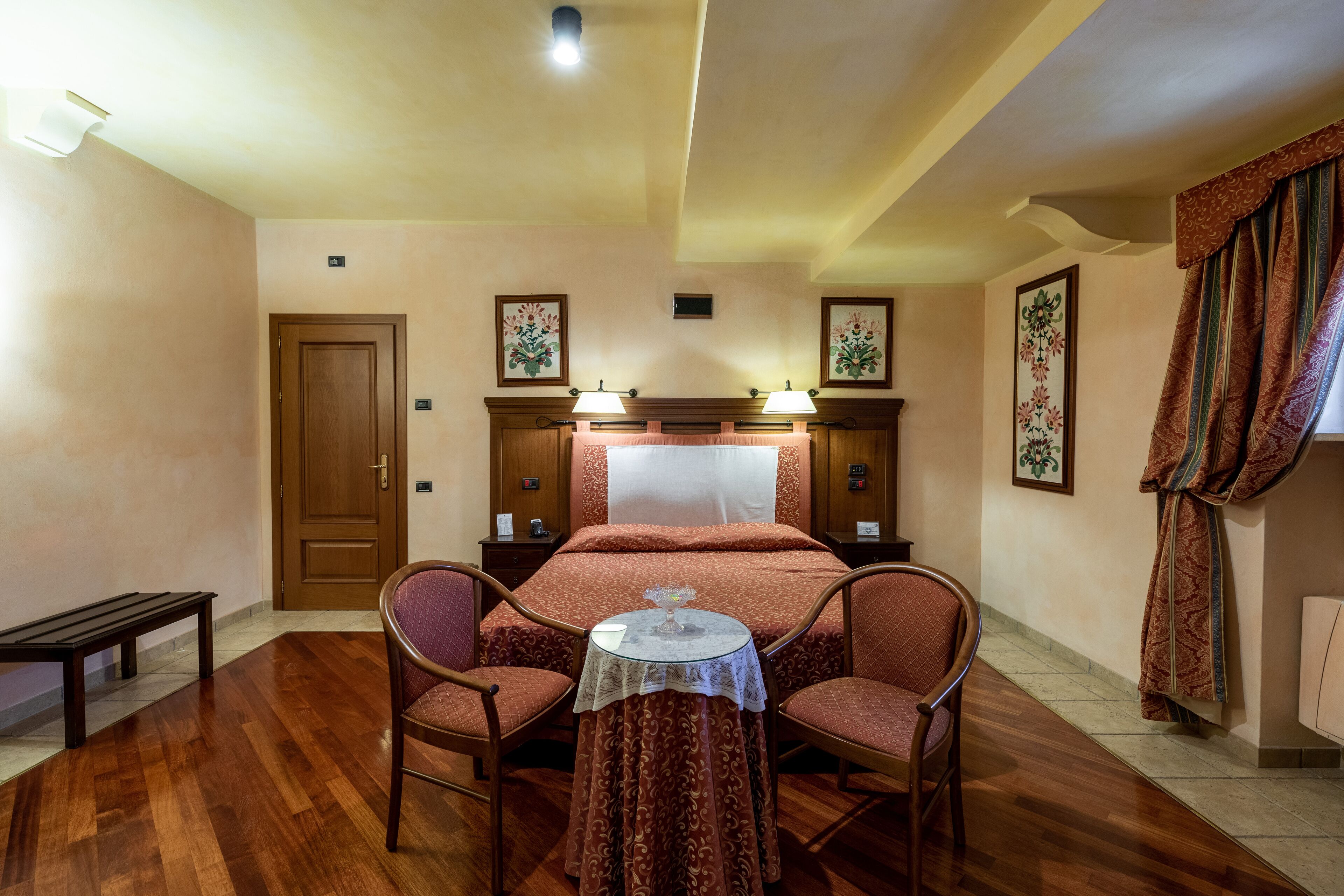A bedroom with a bed, two chairs, a small table, a bench, and a door.