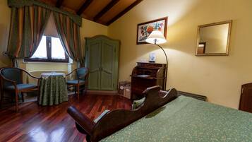 Una habitación con una cama, dos sillas, una mesa, una lámpara, un aparador y un armario.