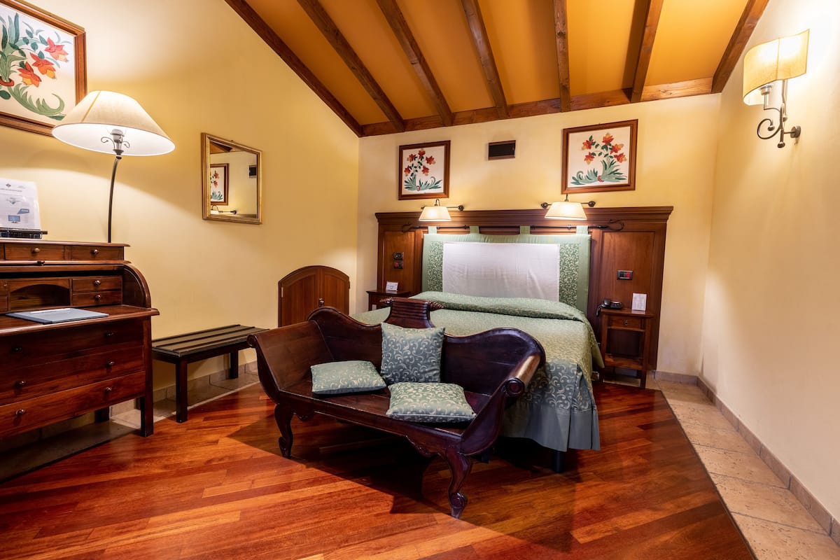 A bedroom with a wooden bed, a bench, a desk with drawers, and a lamp.