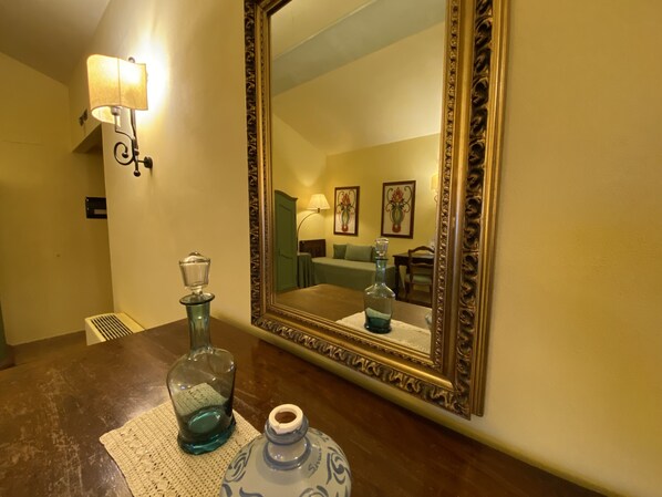 A bathroom with a wooden vanity, a mirror with an ornate frame, a wall-mounted lamp, and a decorative vase. - Relais Santa Anastasia (Castelbuono)