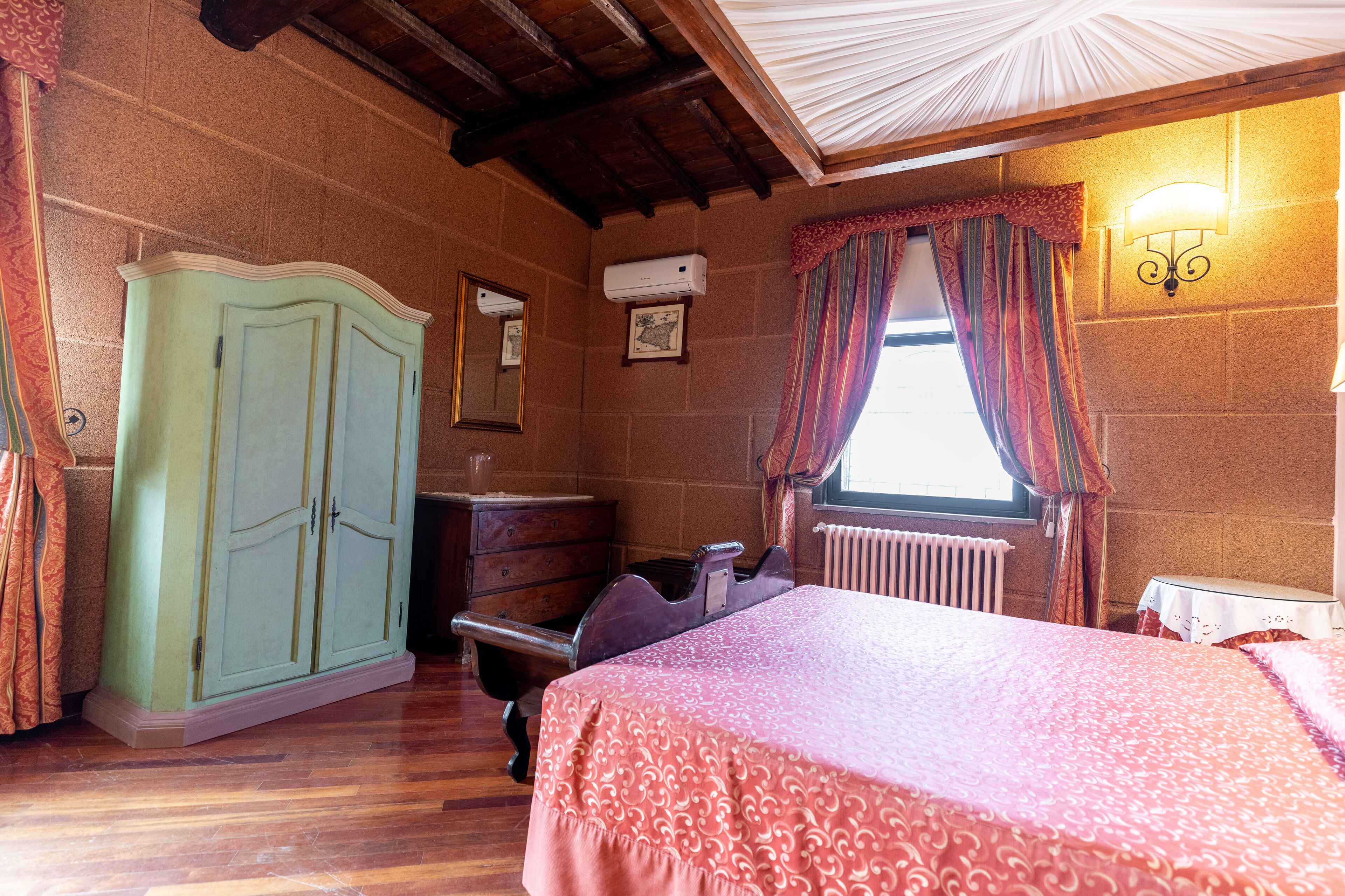 Un dormitorio con cama, cómoda, radiador y ventana con cortinas.