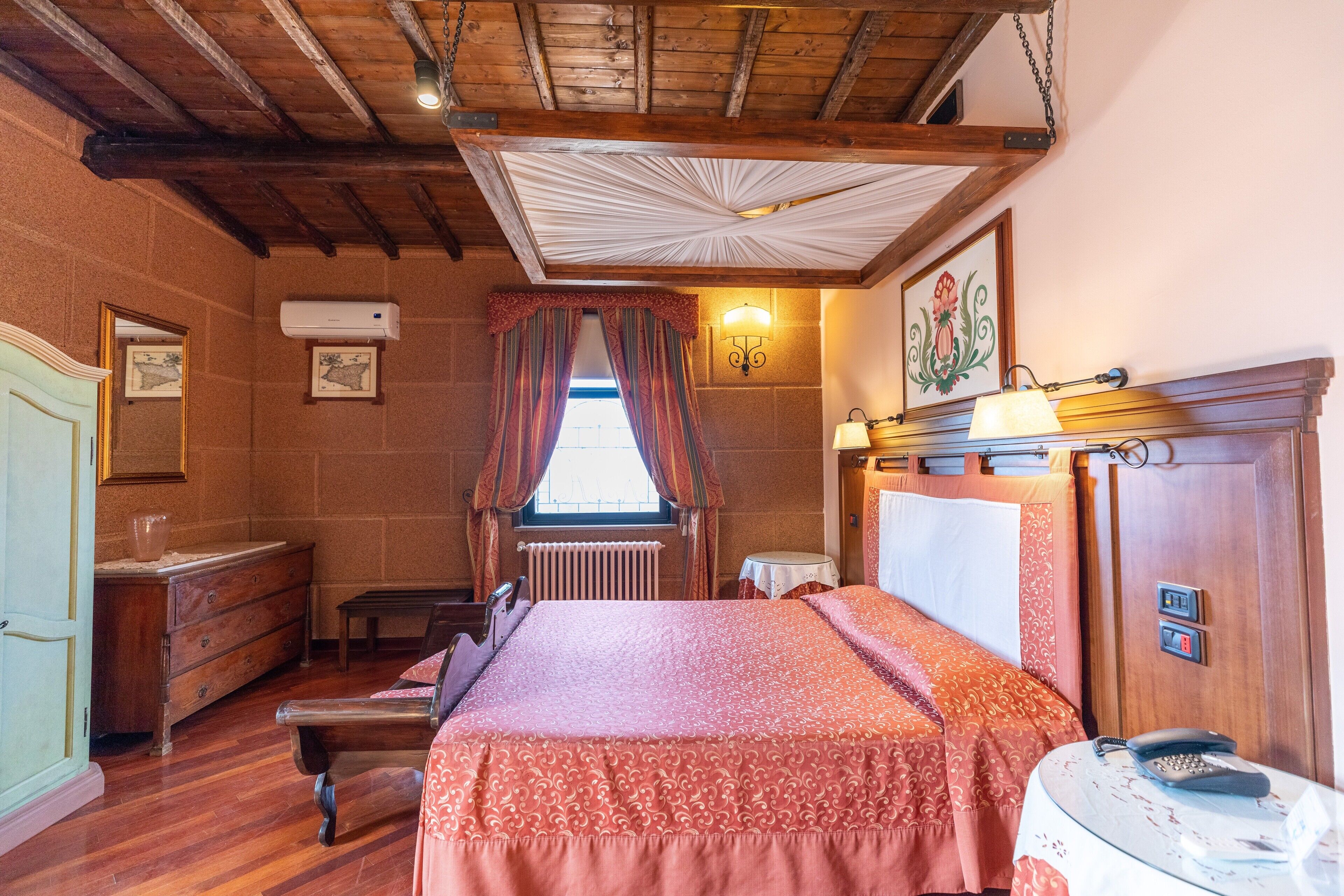 Una habitación con techo de madera, una cama con colcha estampada, un aparador, un espejo y un radiador.