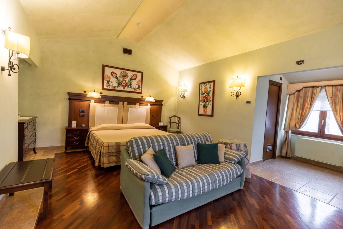 A hotel room with a bed, a sofa, a wooden dresser, and a nightstand.