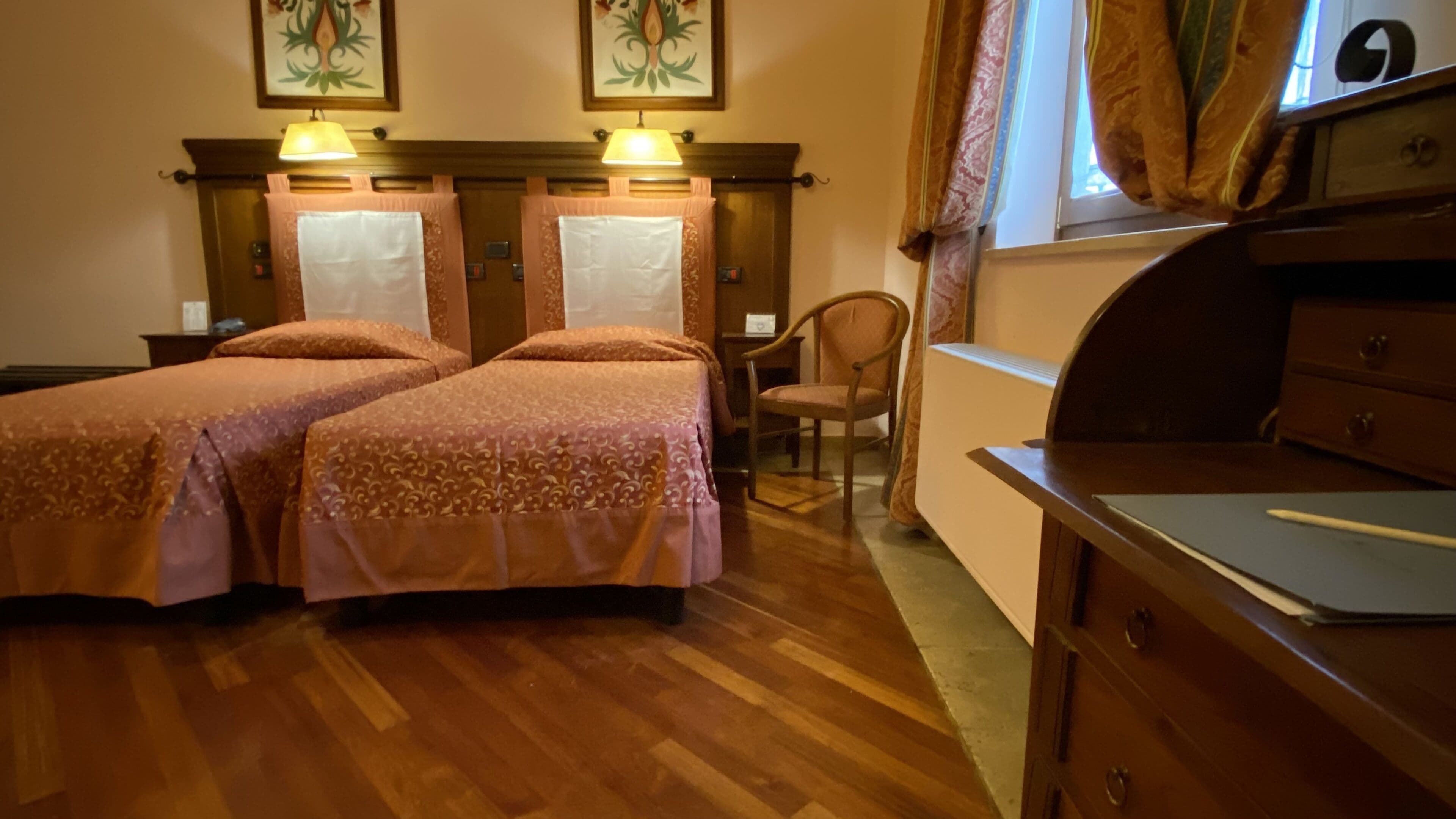 A hotel room with two beds, a wooden dresser, a chair, and a window with curtains.