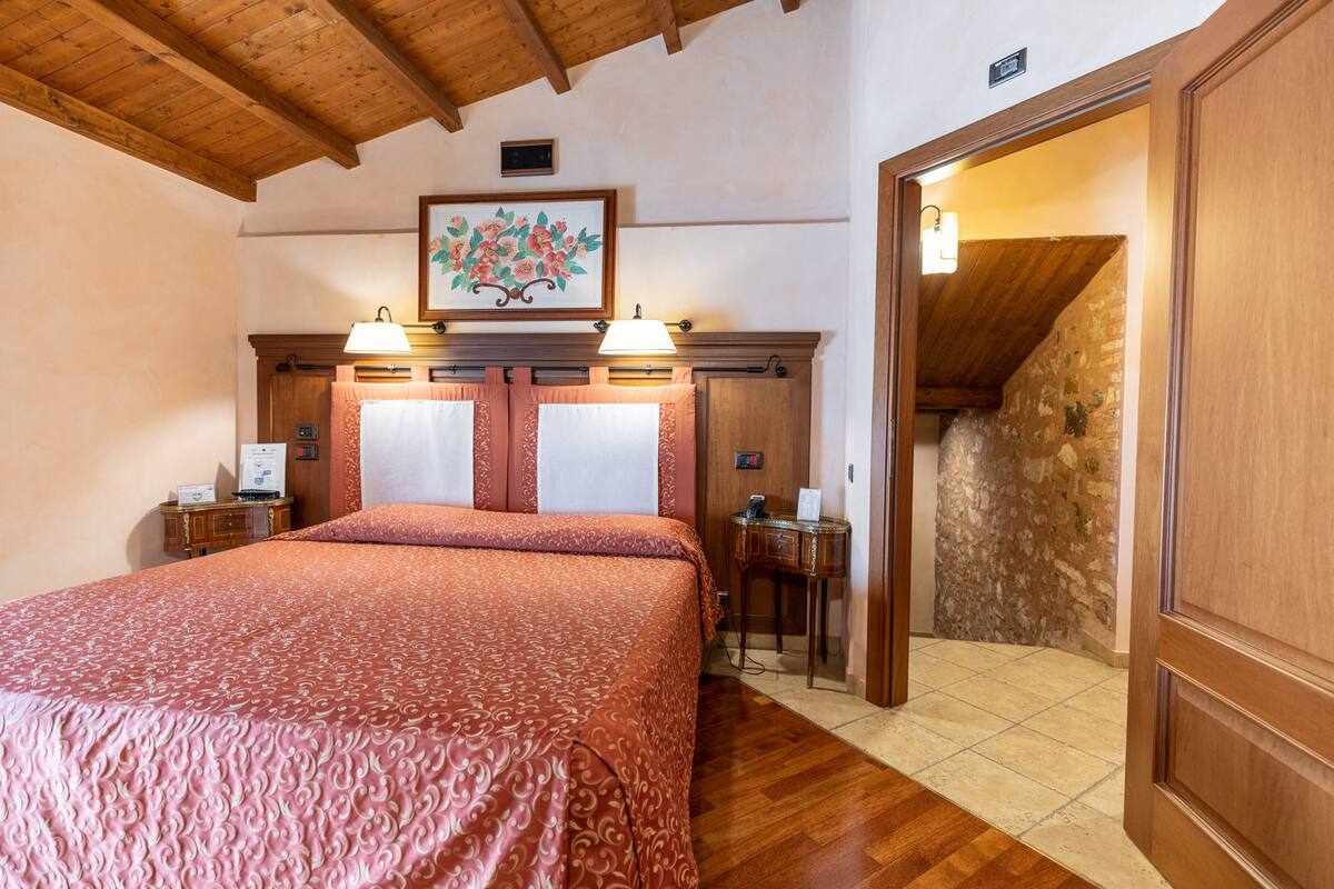A bedroom with a large bed, wooden headboard, two bedside lamps, a nightstand, and a painting on the wall.