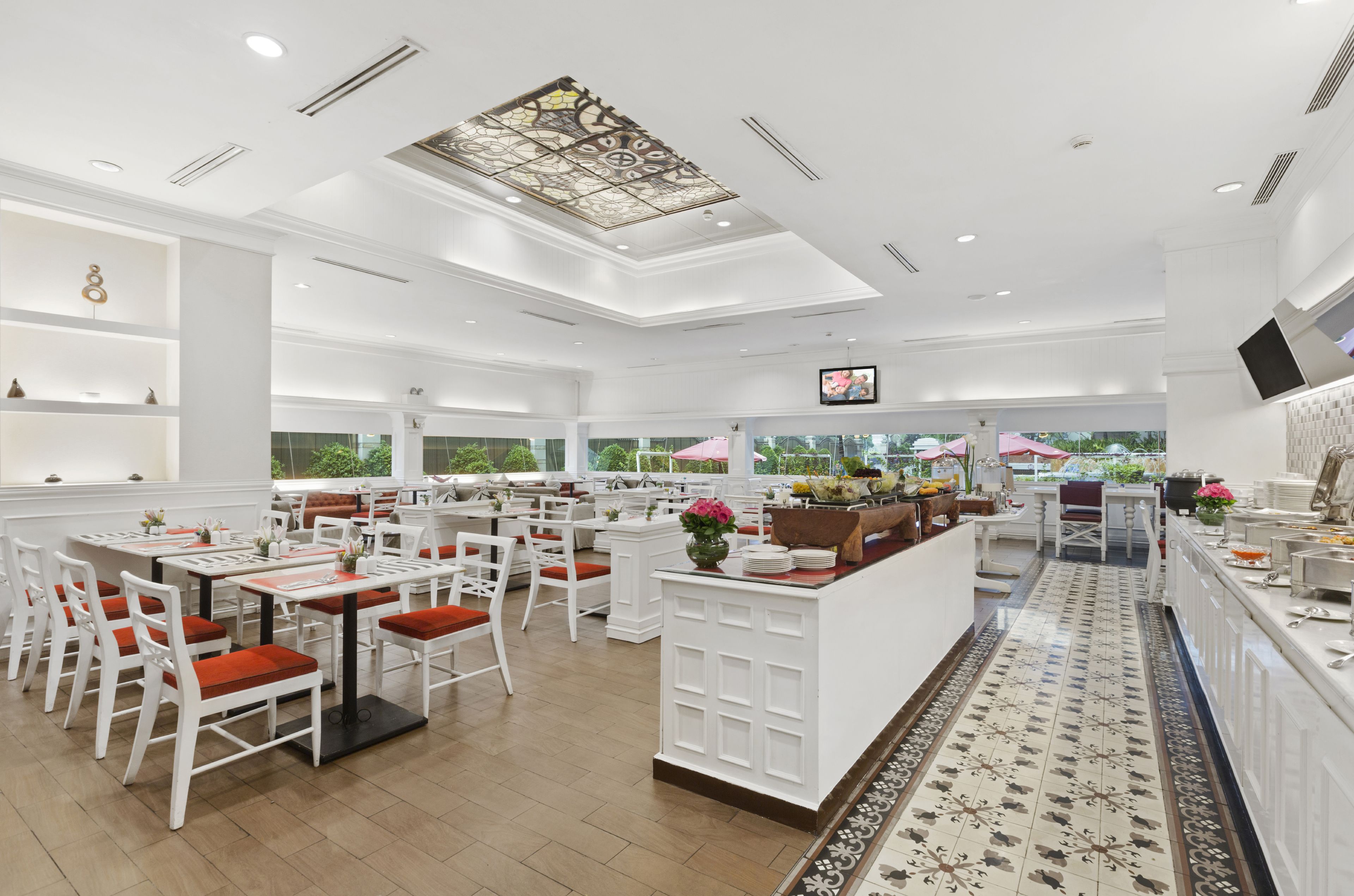 Un restaurante espacioso con mobiliario blanco, una isla central y un amplio ventanal con vistas a la vegetación.