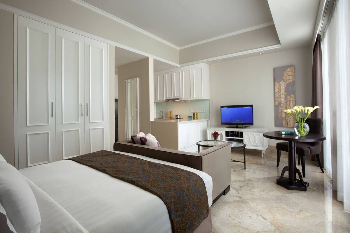 Habitación de hotel con una cama grande, una kitchenette pequeña, un televisor y un comedor con mesa y sillas.