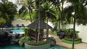 An indoor swimming pool with a thatched gazebo, lounge chairs, and tropical plants. - Ascott Jakarta (Jakarta)