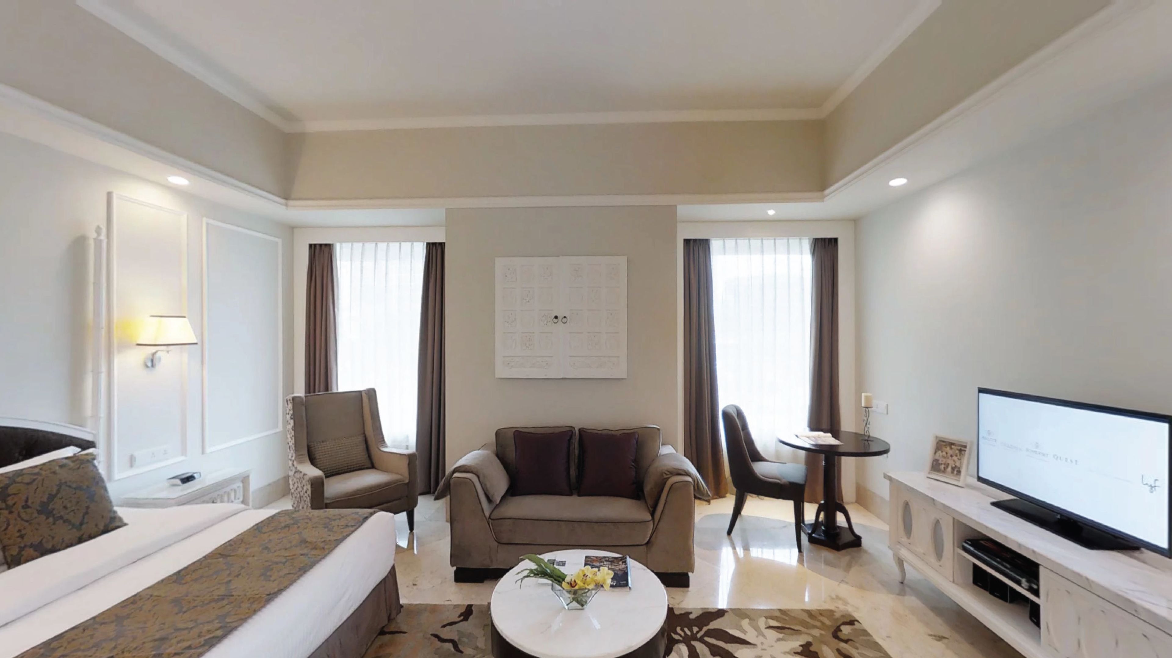 A modern hotel room with a sofa, armchair, and a small round table with a vase of flowers.