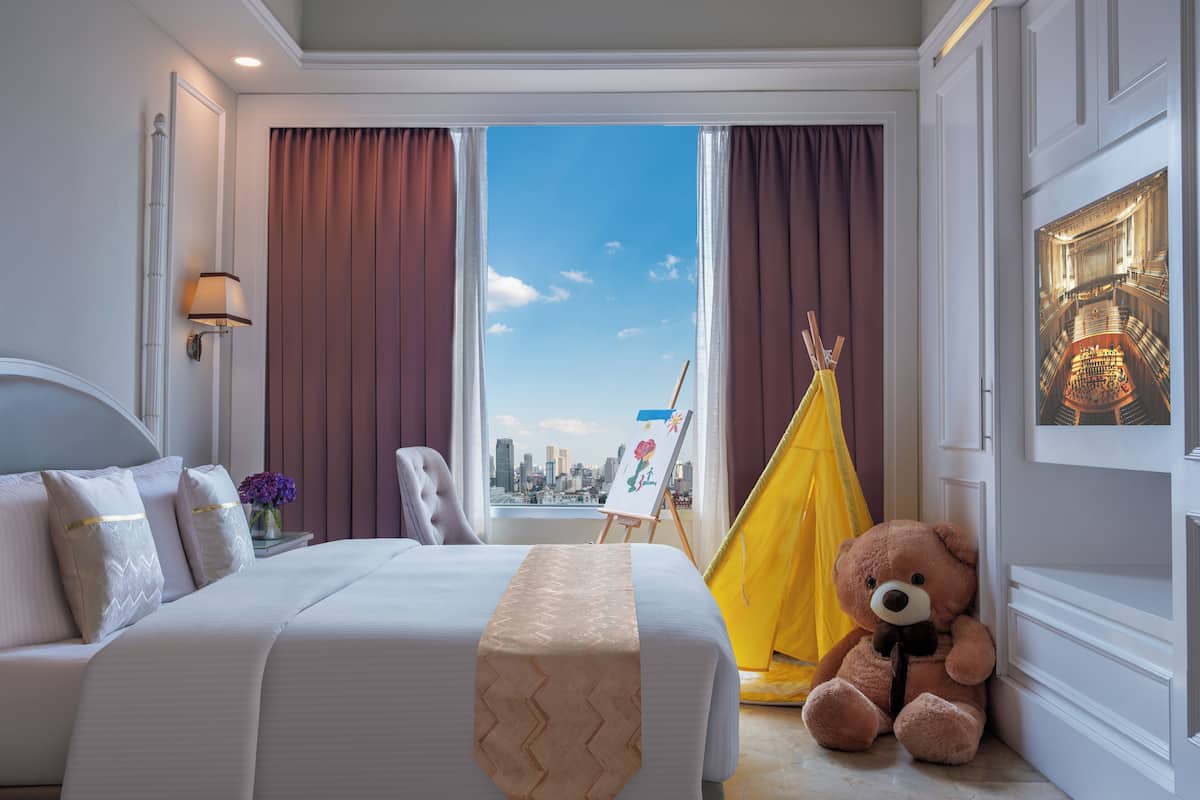 Una habitación de hotel con una cama, un peluche, un tipi amarillo y un cuadro de un paisaje urbano.