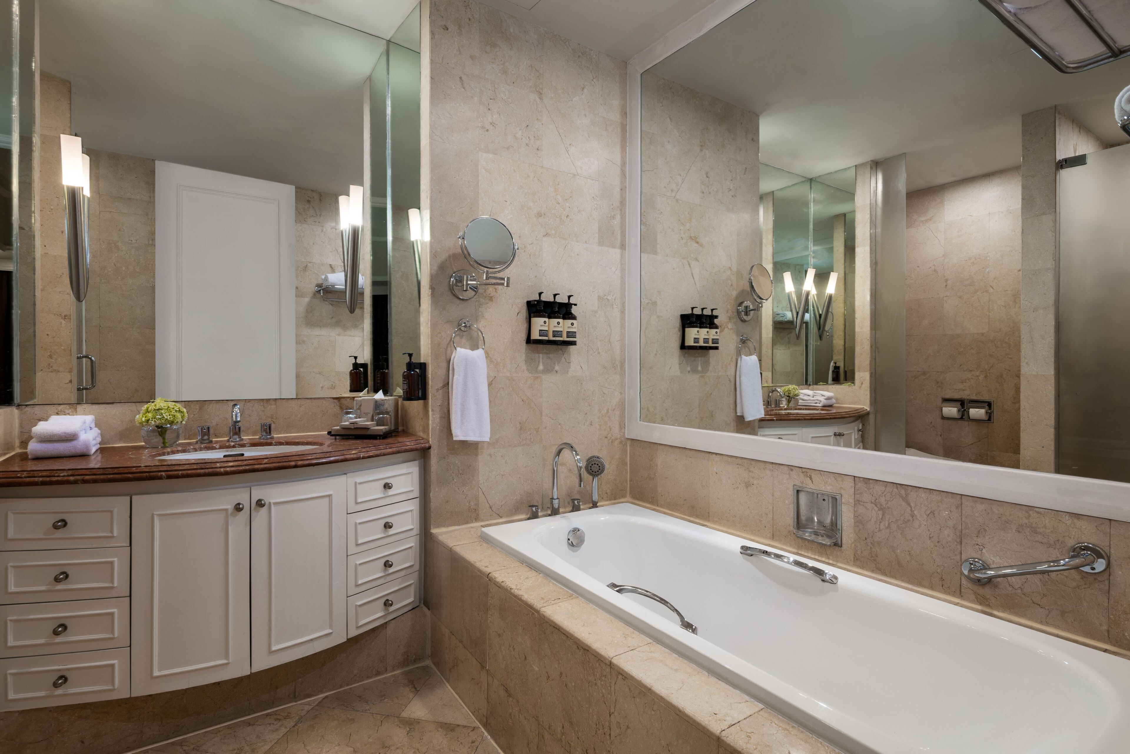 A modern bathroom with a large mirror, a bathtub, and a vanity with a sink and towel rack.