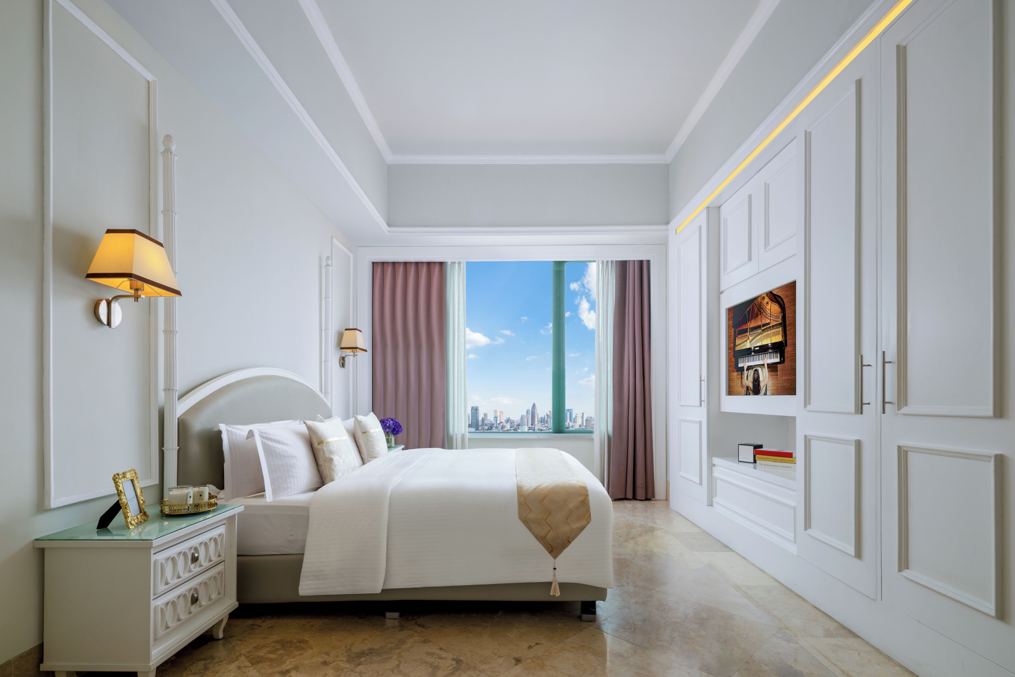 A hotel room with a bed, a nightstand, a lamp, a TV, and a view of the city skyline.