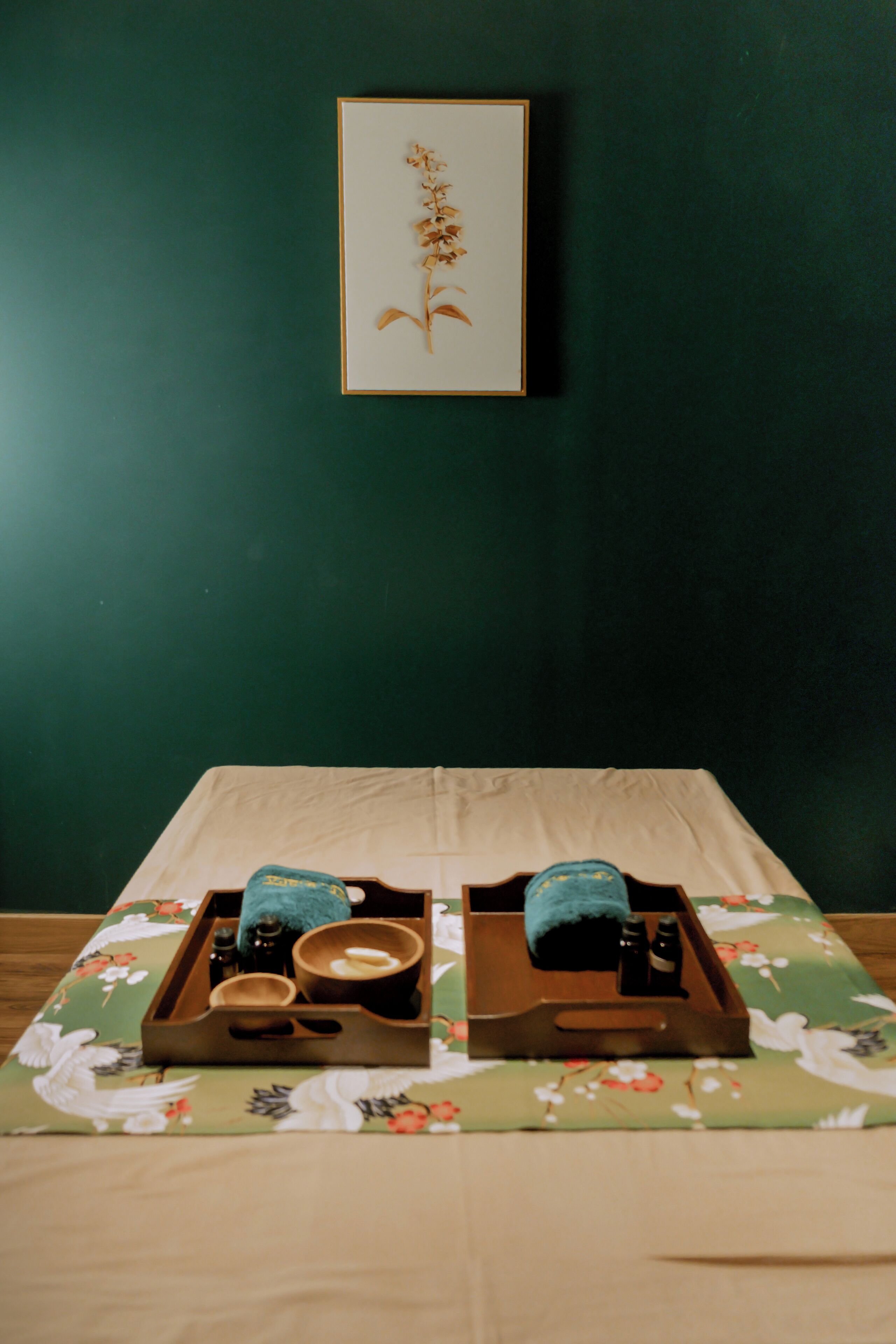 A neatly made bed with a floral-patterned bedspread, a tray with toiletries, and a framed picture on the wall.