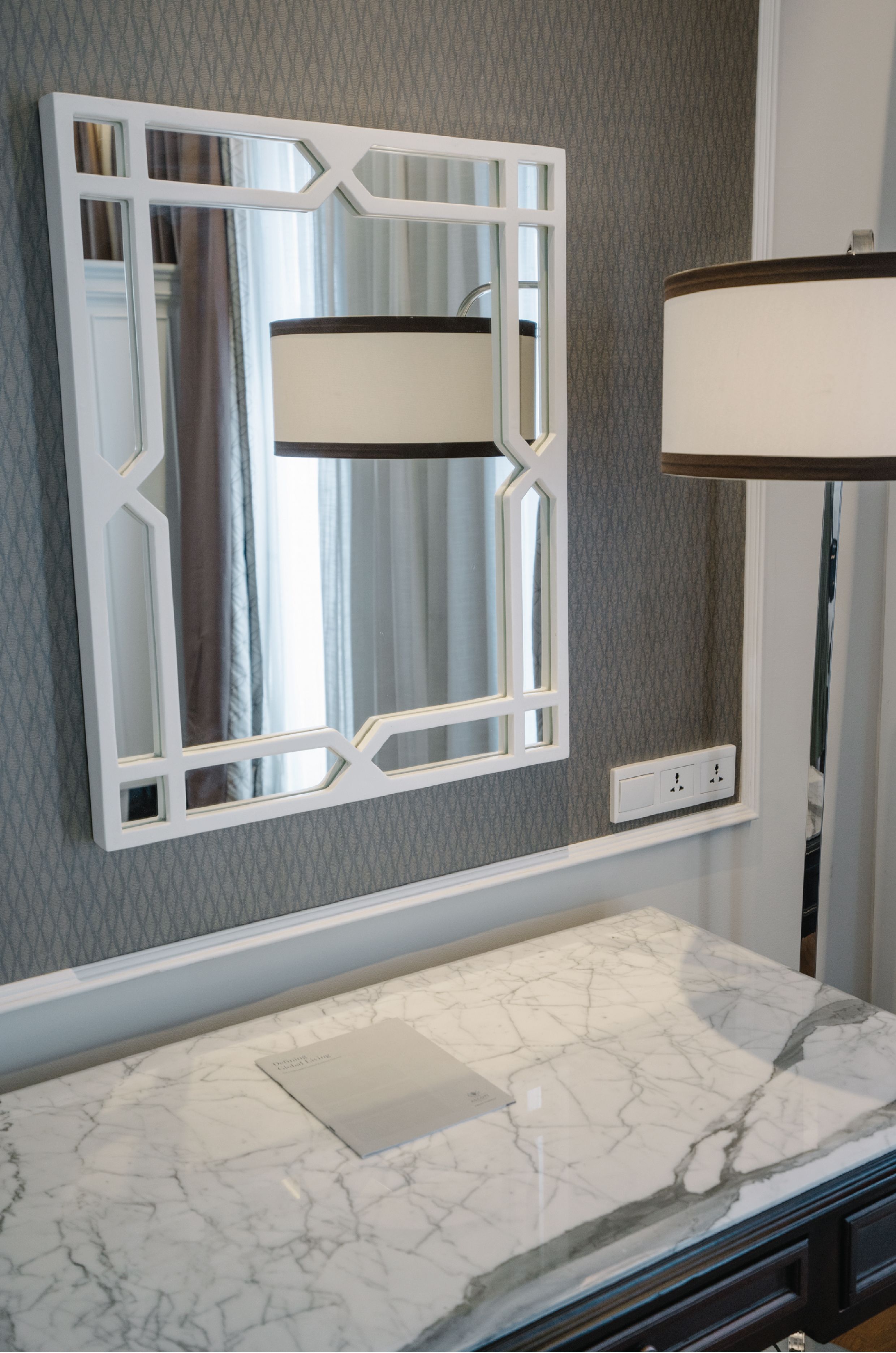 A bathroom with a marble sink, a decorative mirror, and a wall-mounted light fixture.