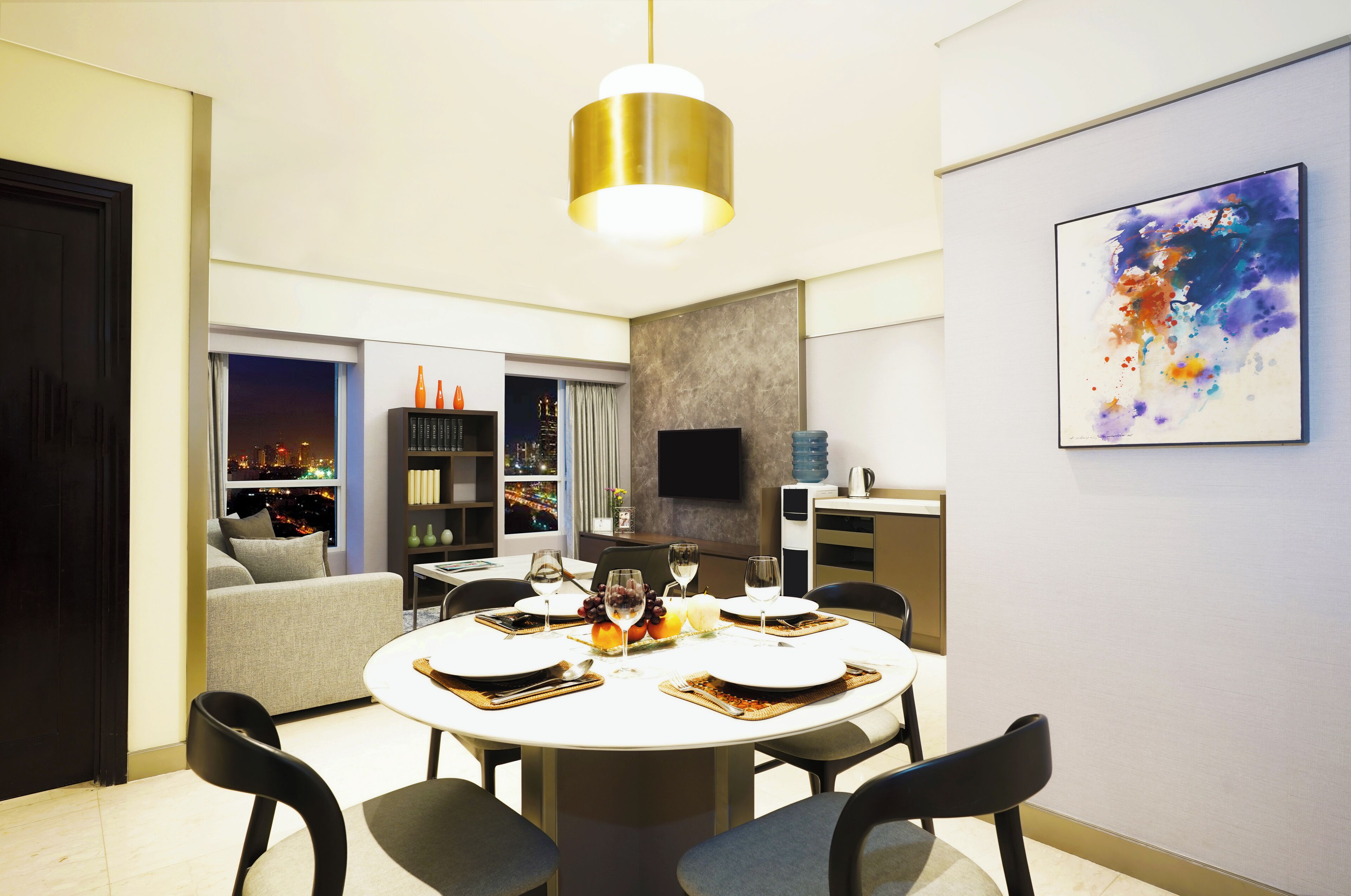 A modern dining area with a round table set for four, surrounded by chairs. A large, modern pendant light hangs above the table.