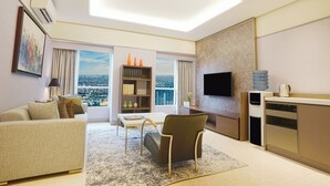 A modern living room with a sofa, a coffee table, a chair, a bookshelf, a flat-screen TV, and a kitchen area with a water dispenser. - Somerset Berlian Jakarta (Jakarta)