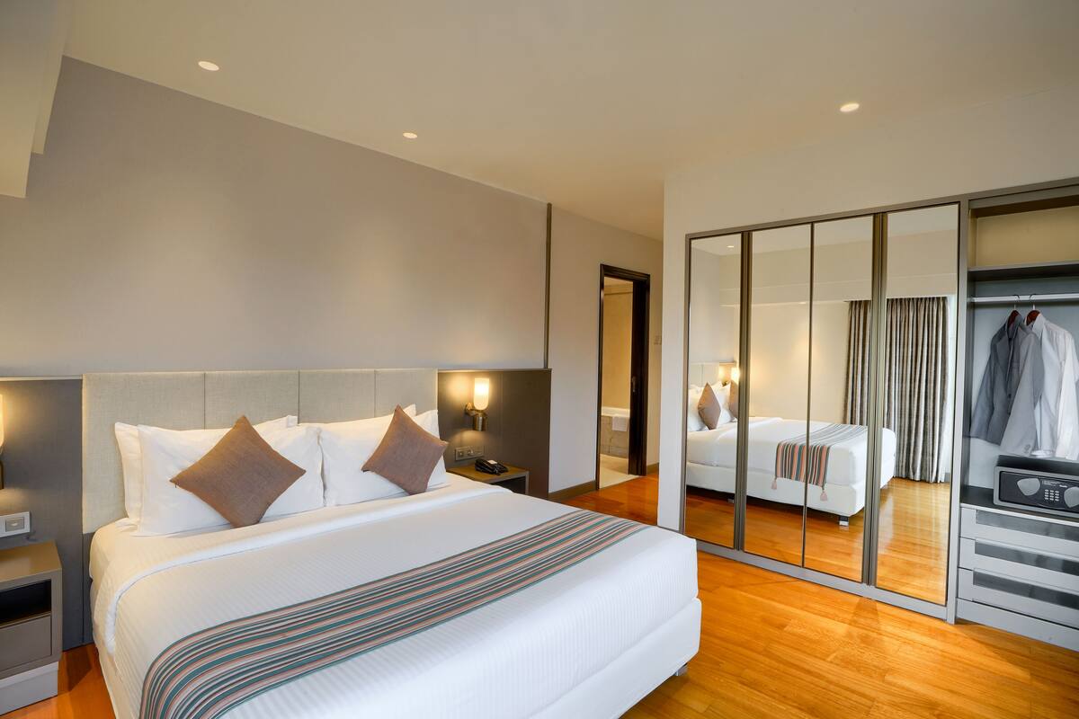 Een hotelkamer met een groot bed, een kledingkast, een spiegel en een nachtkastje met een lamp.