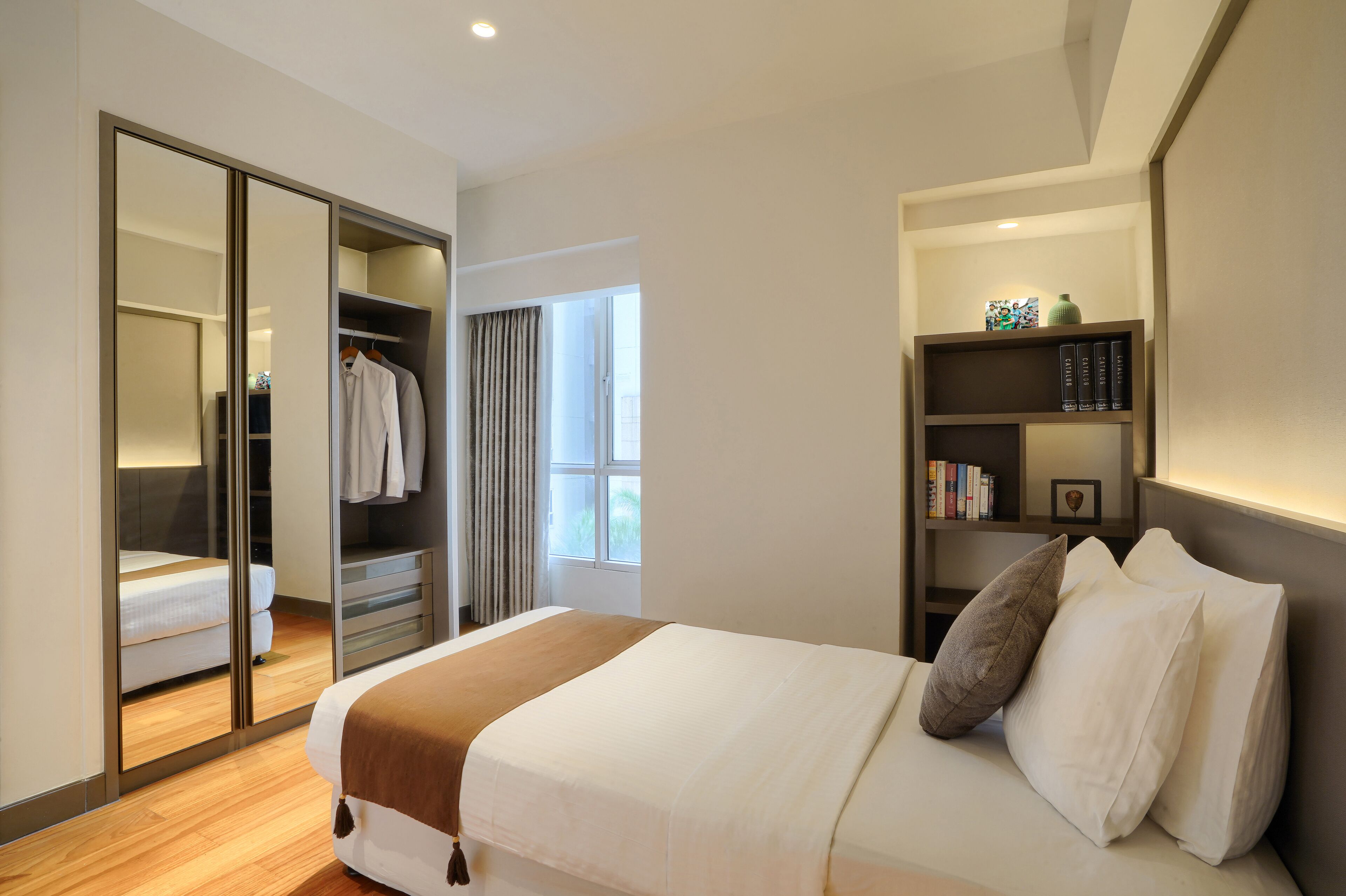A hotel room with a bed, a wardrobe, a bookshelf, and a window.