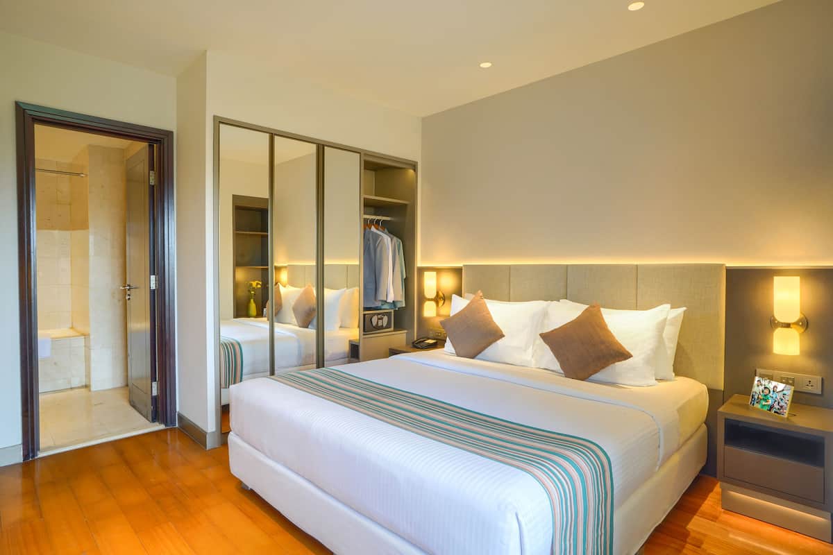 Een hotelkamer met een groot bed, een inloopkast, een badkamer met douche, en een nachtkastje met lamp.