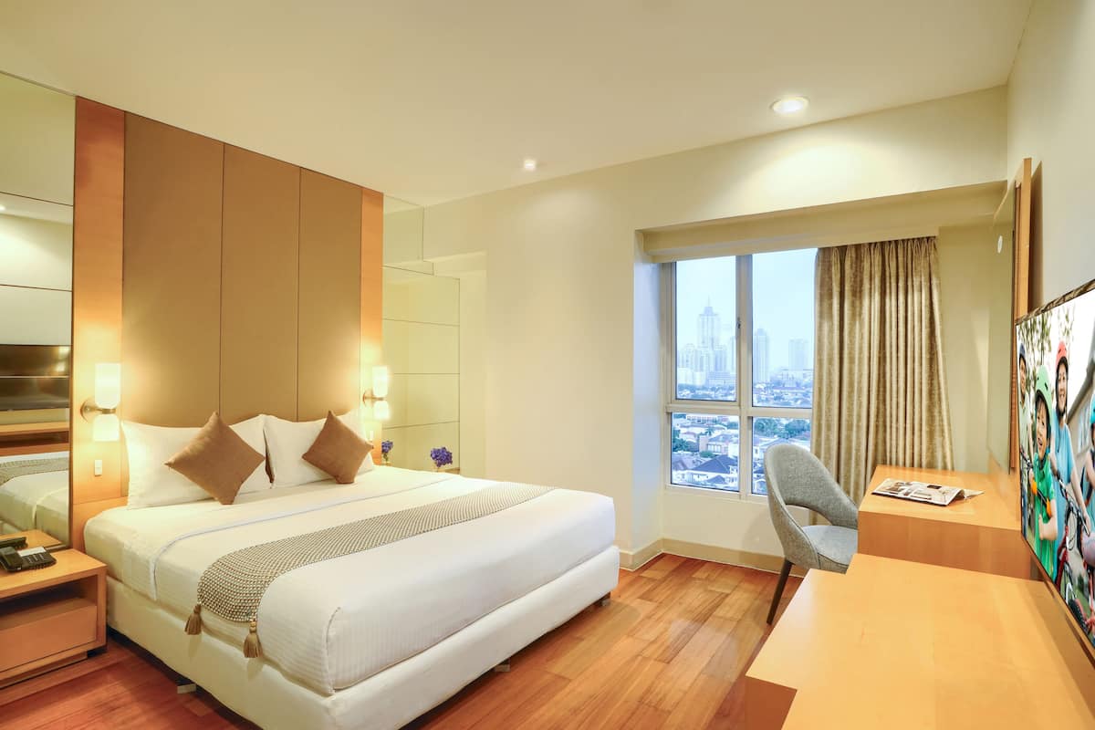 Hotelkamer met groot bed, bureau, stoel, raam met uitzicht op de stad en schilderij aan de muur.