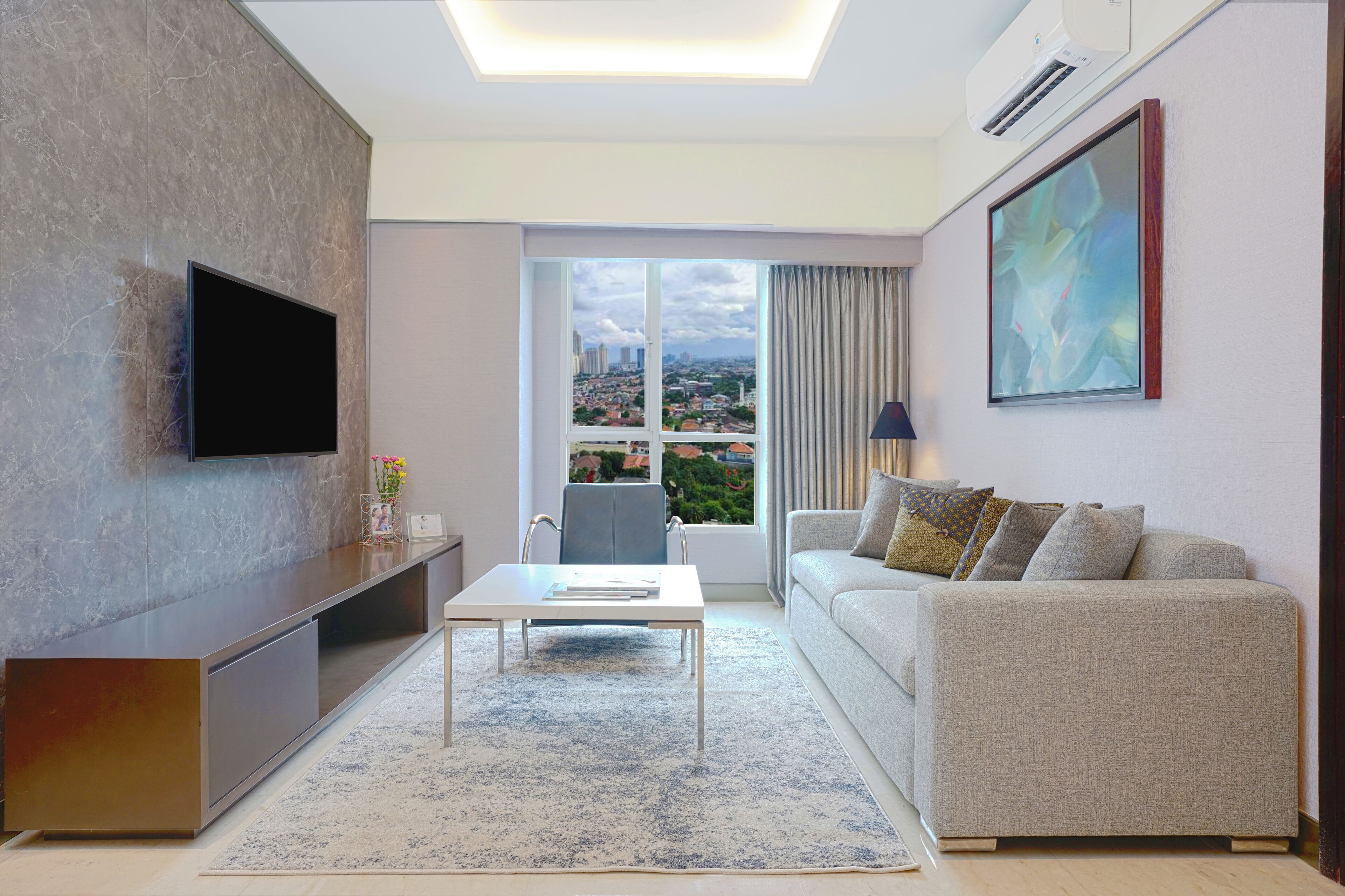 A modern living room with a flat-screen TV, a sofa, a coffee table, and a large window with a city view.