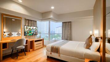 Habitación de hotel con cama, escritorio, silla, televisor y un amplio ventanal con cortinas.