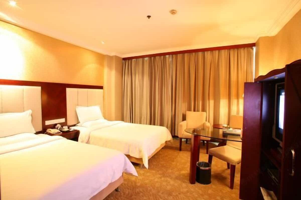 A hotel room with two beds, a desk, a chair, a television, and a curtain.