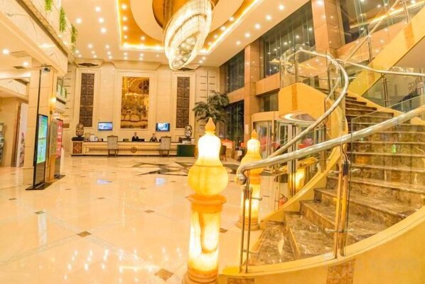 A hotel lobby with a reception desk, a staircase, and a chandelier.
