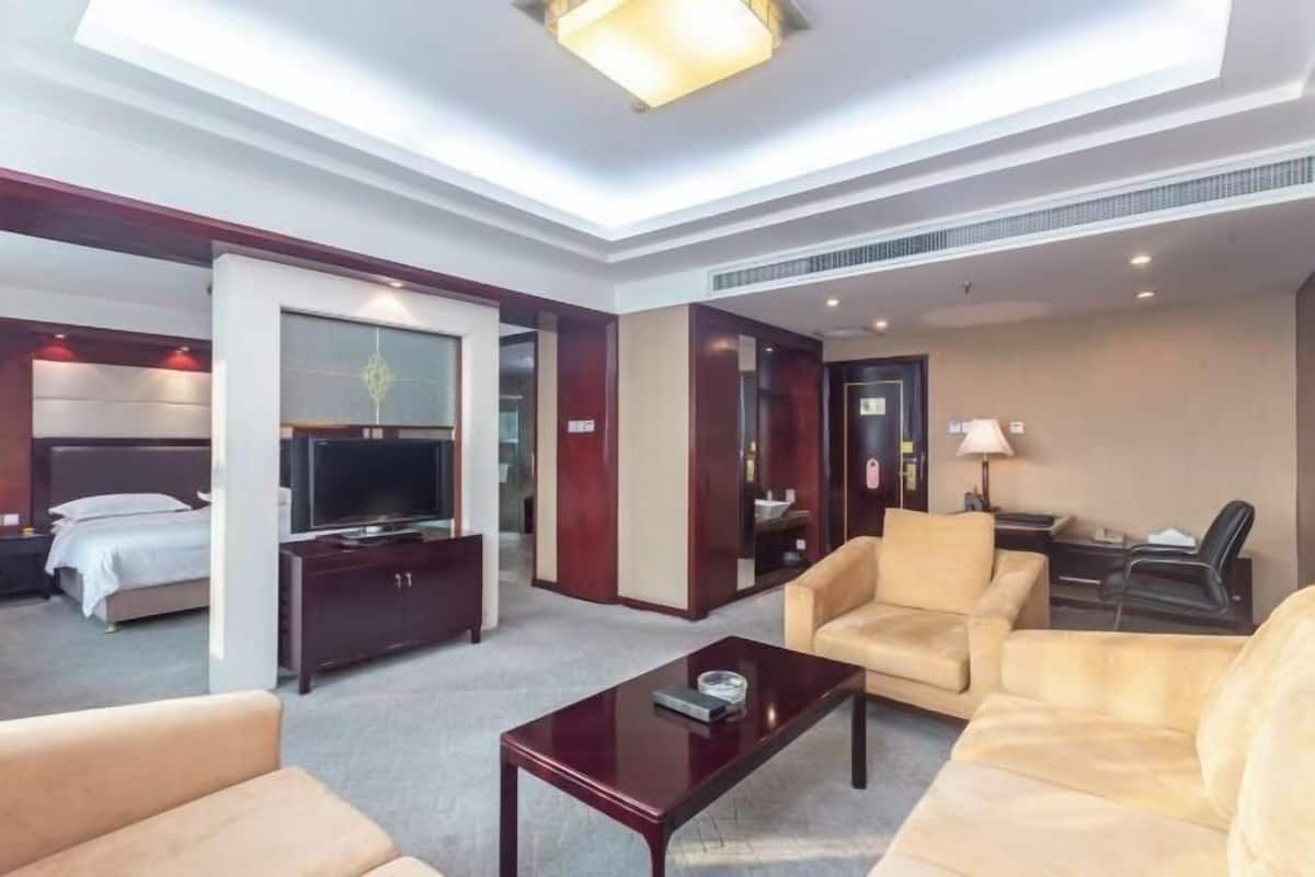 A hotel room with a bed, a TV, a sofa, a coffee table, and a desk with a lamp.
