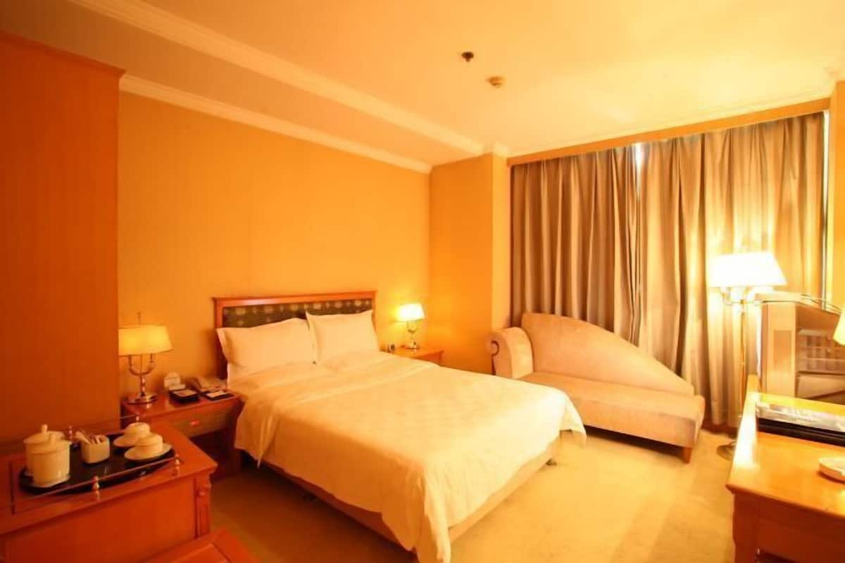 A hotel room with a bed, a chair, a desk with a lamp, and a nightstand with a lamp and a phone.
