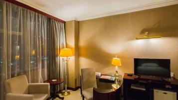 Ein Hotelzimmer mit einem Bett, einem Schreibtisch mit Lampe, einem Fernseher und einem Sessel.