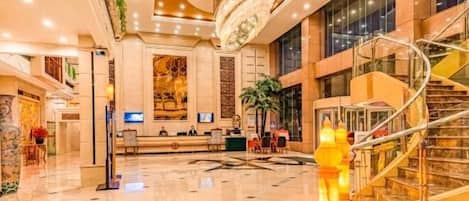 A spacious lobby with a reception desk, a chandelier, and a spiral staircase.