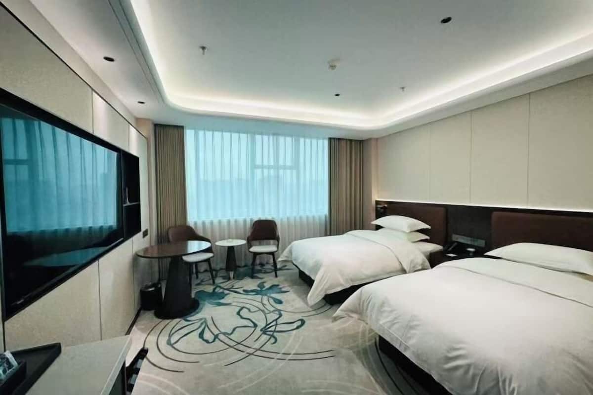 A hotel room with two beds, a TV, a desk, and a chair.