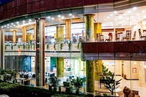 A multi-level hotel lobby with glass walls, multiple seating areas, and indoor plants.
