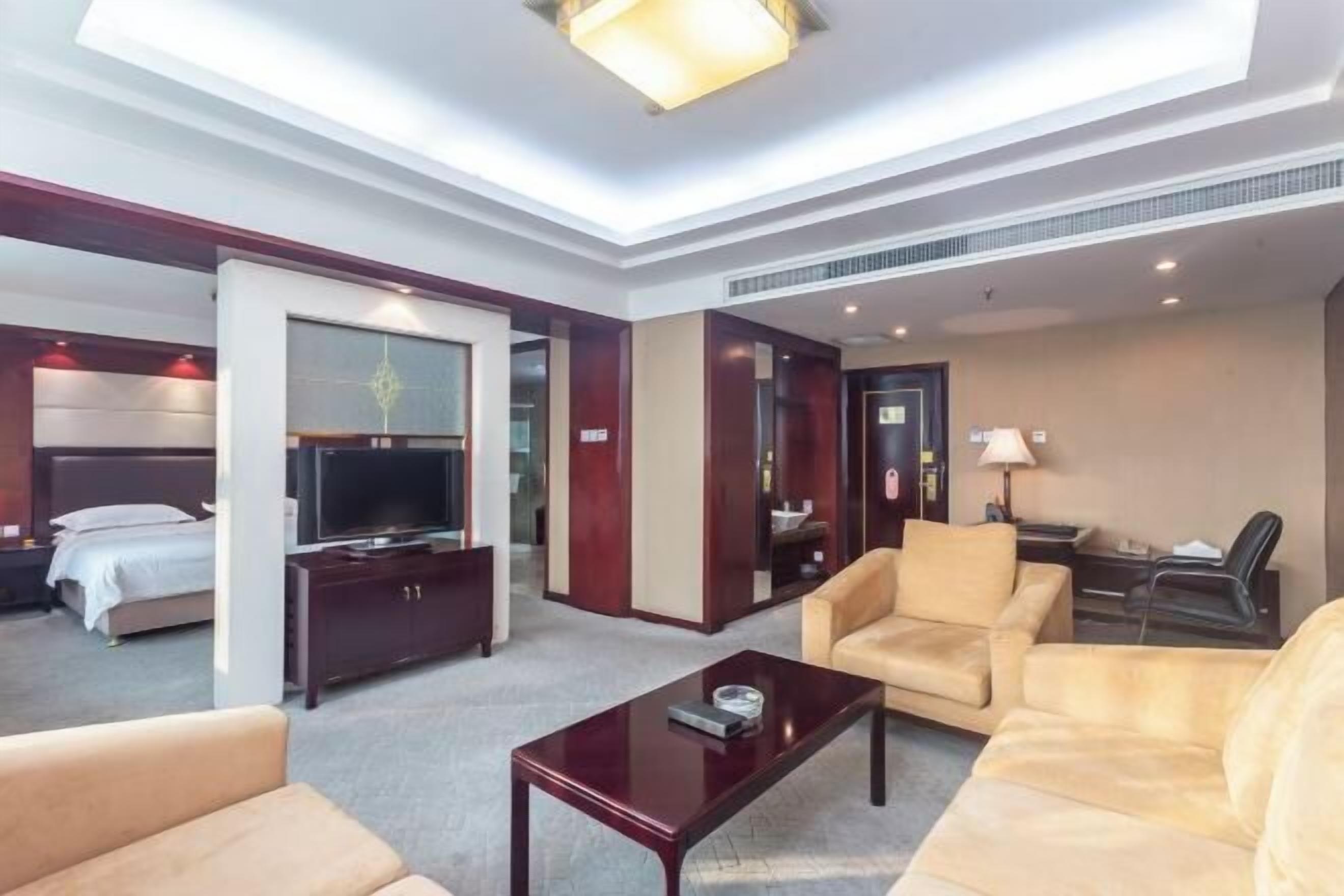 A hotel room with a bed, a TV, a sofa, a coffee table, and a desk with a lamp.