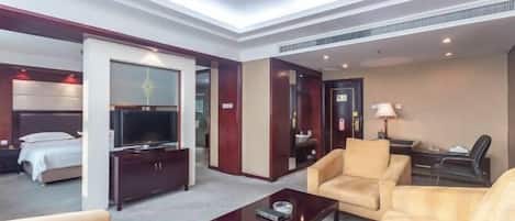 A hotel room with a bed, a TV, a sofa, a coffee table, and a desk with a lamp.