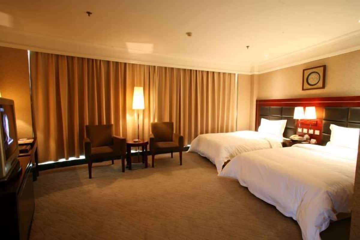 A hotel room with two beds, a TV, a desk, and a chair.