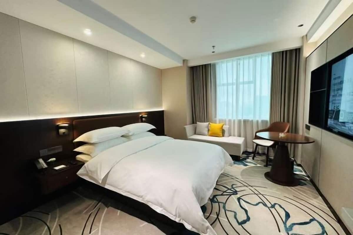 A hotel room with a large bed, a small table, a sofa, and a TV.
