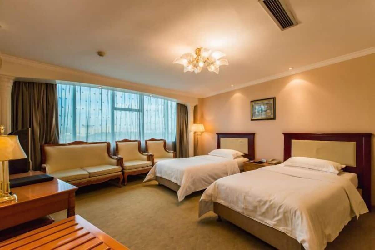 A hotel room with two beds, a sofa, a desk, and a chandelier.