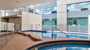 En indendørs swimmingpool med krystalklart, blåt vand, omgivet af fliserede vægge og en glasafskærmning.
