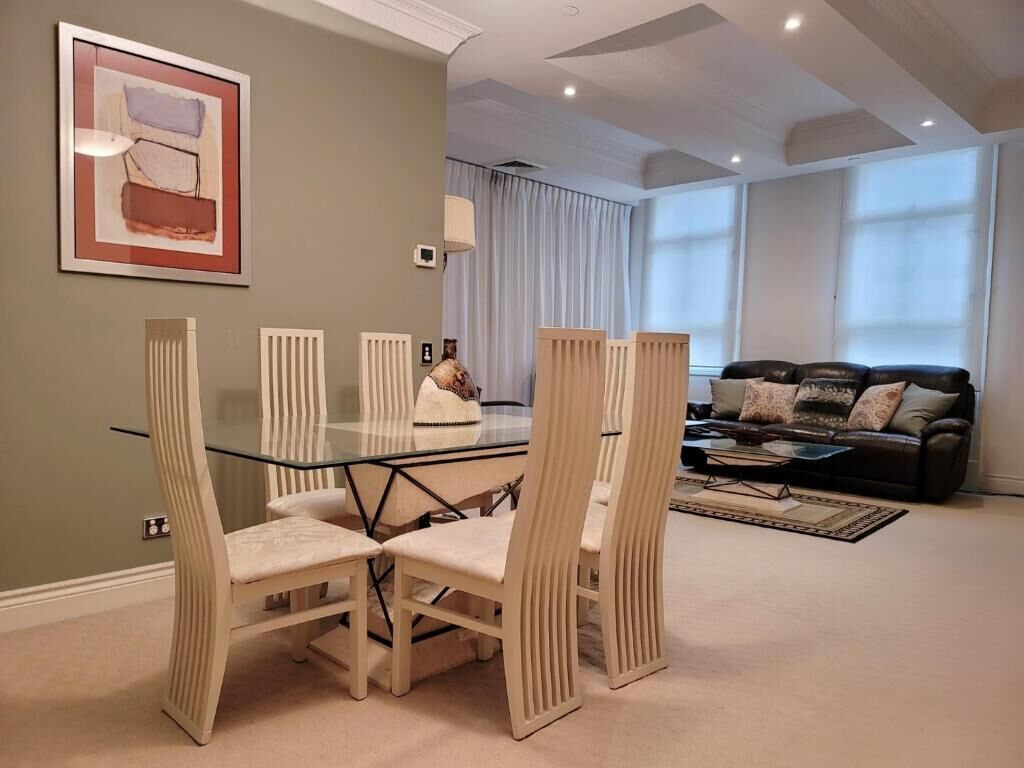 Un comedor con mesa y sillas de vidrio, un sofá y un amplio ventanal.