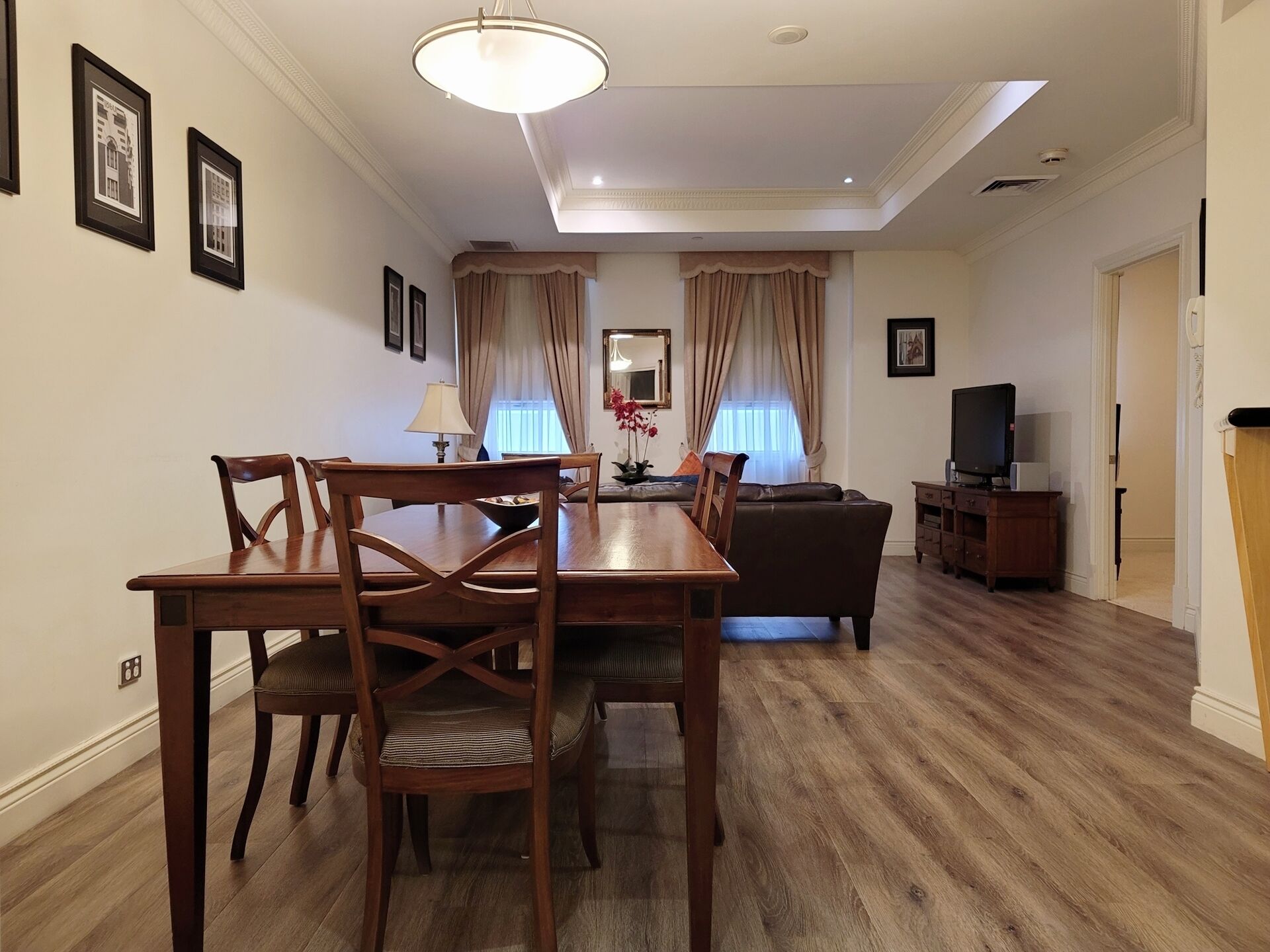 A dining area with a wooden table and chairs, a sofa, a television, and a mirror.