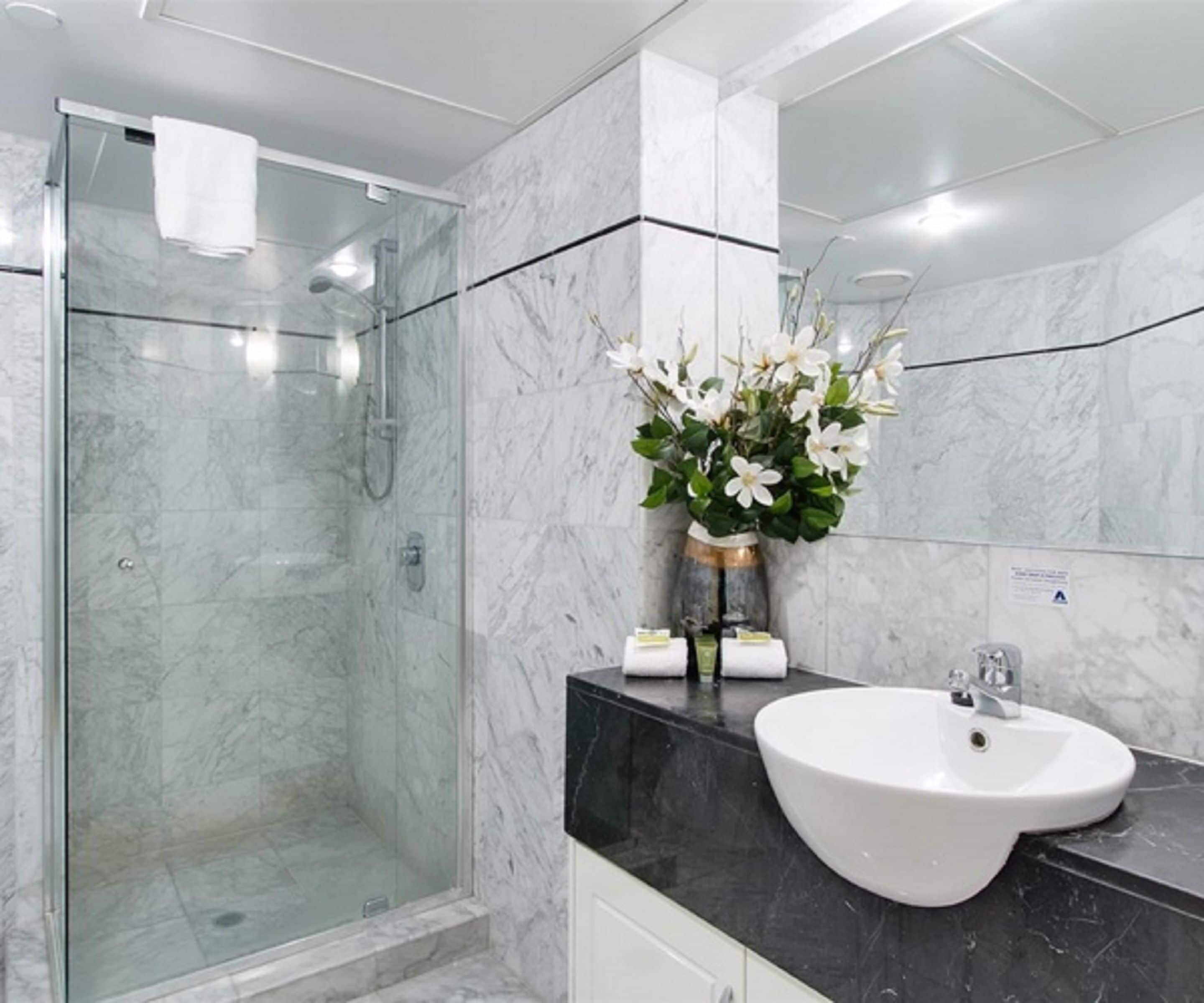 Un baño moderno con ducha envuelta en vidrio, un lavamanos blanco y un florero sobre la encimera.