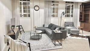 En moderne stue med en hjørnesofa, et rundt sofabord, et fjernsyn og en reol.