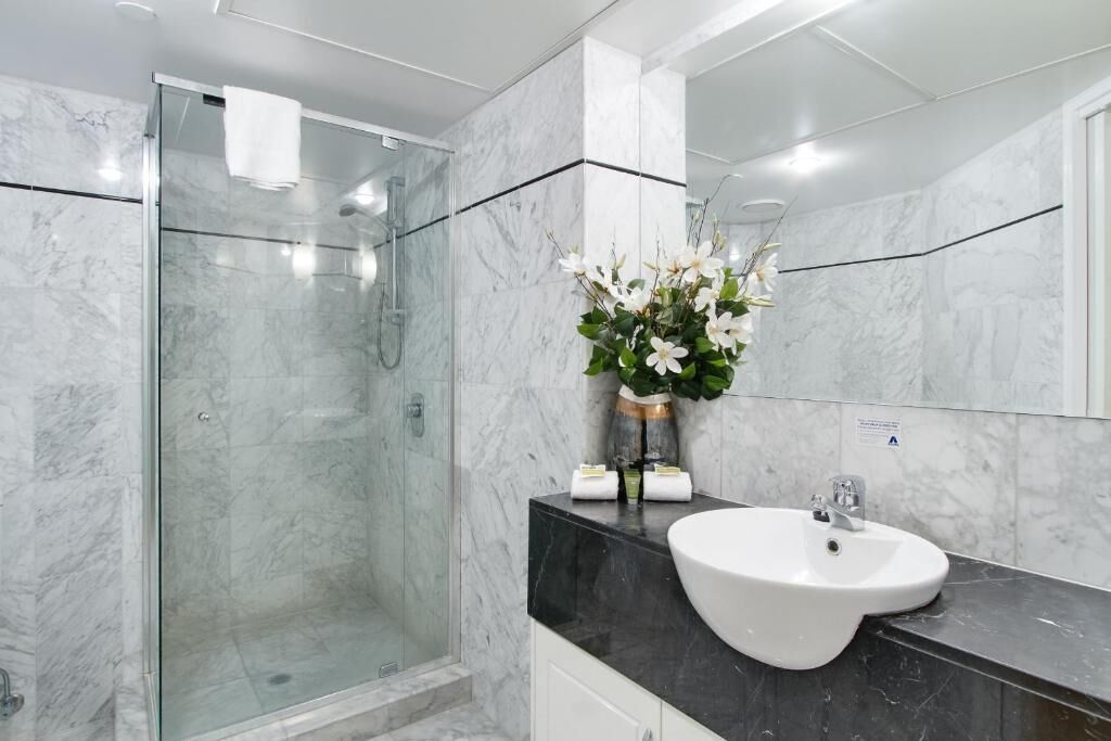 Un baño moderno con cabina de ducha de vidrio, un lavabo blanco y un florero con flores.