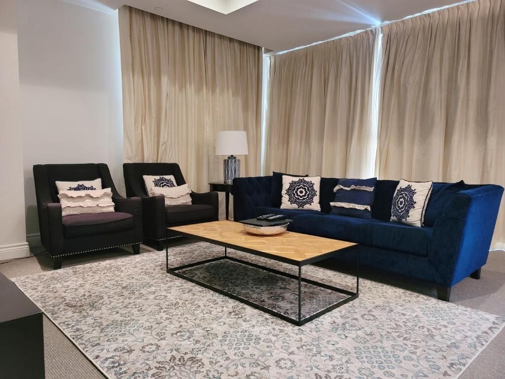 A living room with a blue sofa, two black armchairs, a wooden coffee table, and a patterned rug.