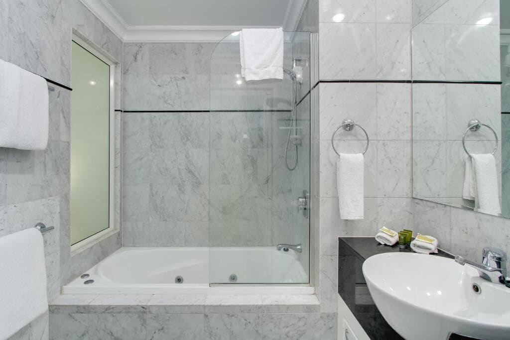 A modern bathroom with a glass-enclosed shower, a separate bathtub, a large sink, and marble walls.